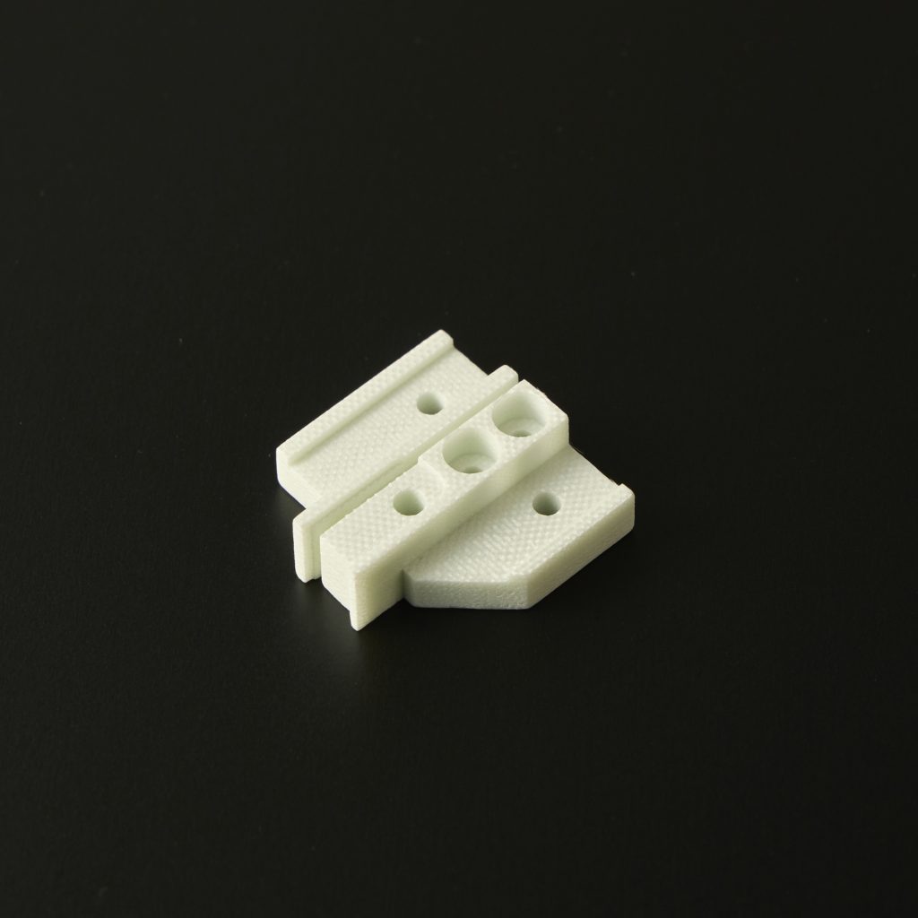 段付きの形状に複数の小径穴をあけた白色プラスチックの精密加工品