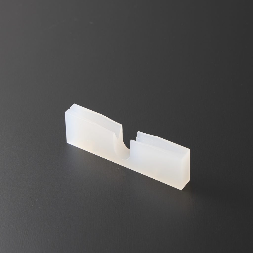 中央に段差のある切り欠きを入れた白色プラスチックの摺動・ガイド部品