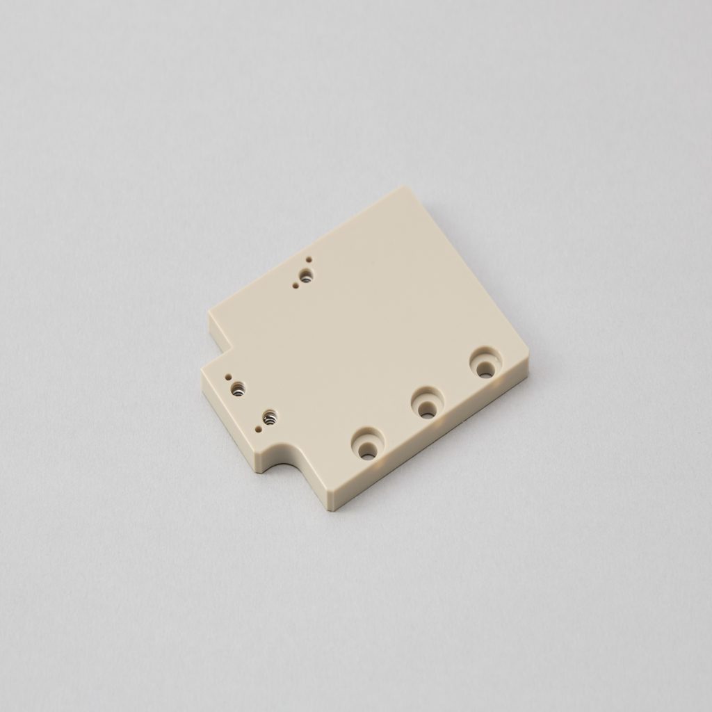 長方形の窓抜きとネジ穴加工が施された黒色樹脂のプレート部品