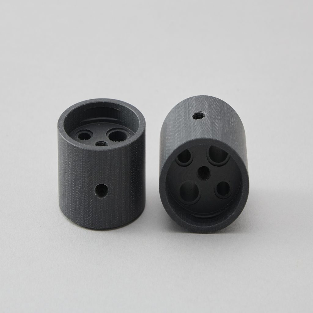 段付きの形状に複数の小径穴をあけた白色プラスチックの精密加工品